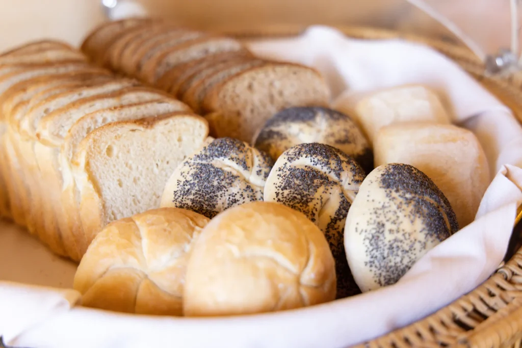 Nell'immagine un cestino contenente delle fette di pane e dei panini rotondi per la colazione